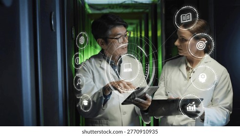 Pointing two technicians in lab coats examining tablets by server racks with green LEDs, AR icons. Datacenter, collaboration, holographic, visualization, professionals, analytics, corridor