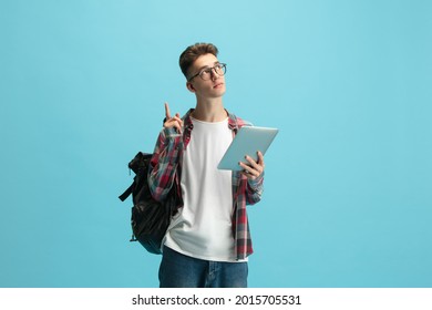Pointing upwards. Young caucasian guy, student in glasses standing with tablet isolated over light blue studio background with copyspace for ad. Concept of education, studying and student life.