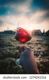 Point-of-View-Shot of a hand holding a glass of red wine into the sun