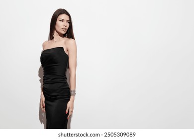 A poised and elegant woman dressed in a stylish black evening gown, set against a minimalist white background, exudes sophistication and grace. - Powered by Shutterstock