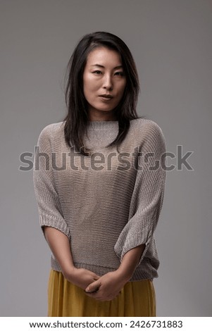 Poised woman in a chic sweater and skirt exudes confidence and a sophisticated air, hands gently clasped