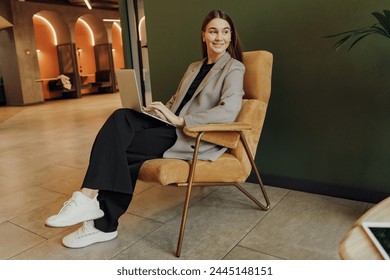 A poised woman comfortably seated in a mustard velvet chair, works on her laptop in a chic, modern lounge, reflecting the fusion of style and functionality.

 - Powered by Shutterstock