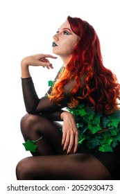 Poison Ivy Comics Character Cosplay. Halloween Costume. Young Sexy Woman In A Vine, Leaves And Poison Ivy Costume Posing As A Superhero Against White Wall Background. Female With Curly Red Hair