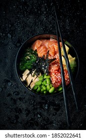 Poke bowl with salmon. Raw fish, beans, avocado, corn, seaweed and rice with chopsticks on a black stone background - Shutterstock ID 1852022641