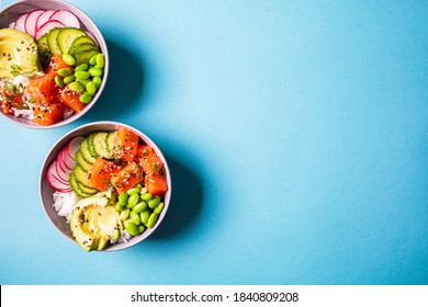 Poke bowl with salmon, rice, avocado, edamame beans, cucumber and radish in a gray bowls, top view. Hawaiian ahi poke bowl, blue background. - Shutterstock ID 1840809208