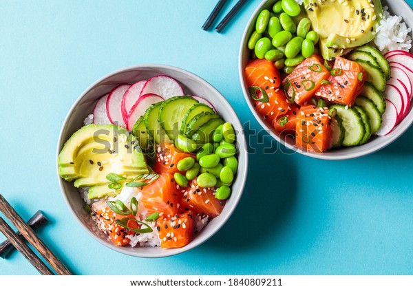 Poke bowl with salmon, rice, avocado, edamame\
beans, cucumber and radish in a gray bowls, top view. Hawaiian ahi\
poke bowl, blue\
background.