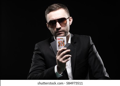 The Poker Player In Black Glasses, In A Casino With Open One Card. On A Black Background.