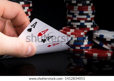 a poker player looks at his cards by raising them on a black table against the background of stacks of poker chips