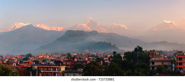 Pokhara cityscape and the magnificent Himalaya mountain range with saint Machapuchare mount in the morning, at dawn. Nepal, horizontal panoramic view with fog and clouds over the city - Shutterstock ID 715733881