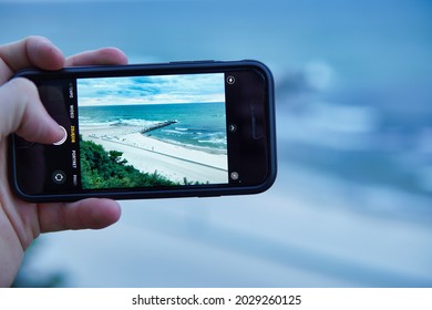 Jarosławiec, Poland - 08.22.2021: A Man Takes A Picture Of The Beach With An IPhone. Taking Photos While On Vacation. Beach In Jarosławiec On The Baltic Sea