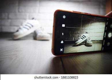 
Bielsko-Biała, Poland - 12.23.2020: The Man Sells Unused Shoes. Selling Old Clothes Online Instead Of Throwing Them Away. A Boy Takes Pictures Of White Shoes Using A Smartphone For An Auction Site