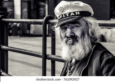 Poland, Gdansk, 06.03.2015 Old man, sailor, with a thick beard and a captain's cap observing ships on the quay. Black and white photo.