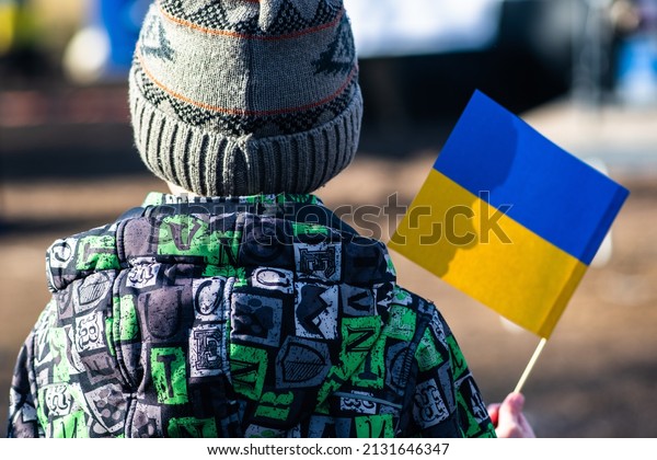 Poland - March 2, 2022: Child or kid with winter\
clothes, hat and Ukrainian flag, profile of the child is on the\
flag. War in Ukraine, caused by Putin and Russia, refugee, refugees\
camp