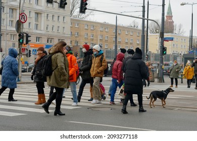Poland Warsaw December 2021. Pedestrians pass in two directions on the crossing, many of them wearing protective masks due to the covid-19 pandemic. In the background, city architecture, traffic light