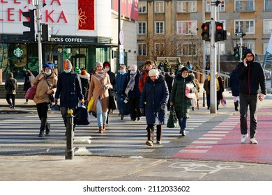 Poland Warsaw Jan 2022. Pedestrian crossing with people. Some wear protective masks because of the covid-19 pandemic, winter clothes. Visible light signaling and fragments of the city's architecture.