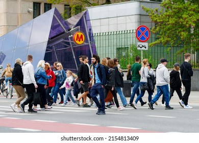 Poland, Warsaw, May 2022. A pedestrian crossing with a crowd, a metro station in the background, the surrounding architecture and the greenery of the city in spring.