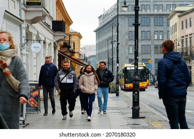 Poland, Warsaw, November 2021. People on the sidewalk in autumn clothes are walking, a few in protective masks due to the covid 19 pandemic. There is a bus on the street, architecture around. Grey day