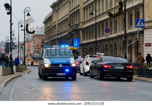 Poland,\
Warsaw, November 2021. A police car driving down the street, other\
cars around, pedestrians, city\
architecture.