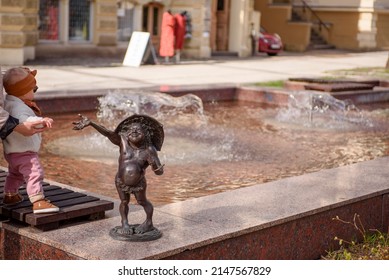 Poland, Zielona Góra, 04.12.2022. Little Fashionista On A Walk In The City Square. Miniature Sculptures Of Bacchus, Presented In An Unexpected Way.