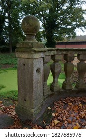 Pole of the balustrade of an old stone bridge covered with moss and lichen. Rustic and romantic environment, breathing the past. Green water covered with duckweed beneath.  