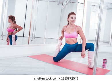 Pole dance studio. Dark-haired slim woman wearing leggings stretching her legs in pole dance studio - Powered by Shutterstock