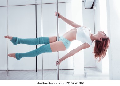 Pole flow. Strong and fit red-haired pole dancer making pole flow while training in light spacious studio - Powered by Shutterstock