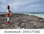 a pole with a lifebuoy in a rocky cove, on a day with overcast sky, lonely volcanic rock beach on a winter day in Lanzarote, Caleton Blanco, horizontal