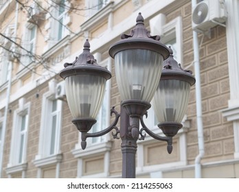 A Pole With Street Lights Off During The Day With A Building In The Background