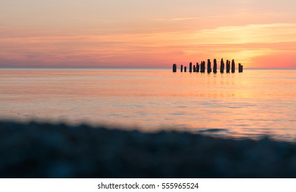 Poles In Still Water, Sunset Beyond Horizon In The Sea