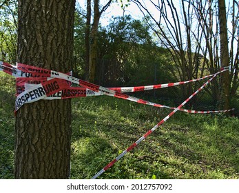 Cinta de barrera policial con rayas rojas y blancas que se extendían entre dos troncos de árboles en una zona verde cerca de la ciudad de Karlsruhe, Baden-Württemberg, Alemania. Texto en alemán: 