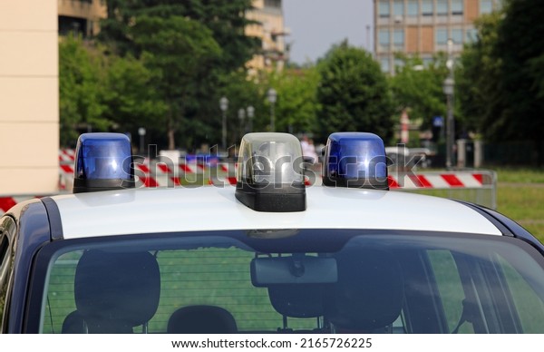 police car with blue lights sirens in the city
with houses and building in
background