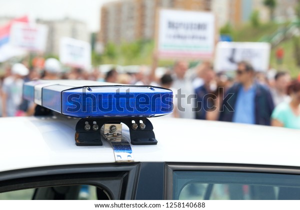 Police car flashing lights in focus, blurred\
protesters in the\
background
