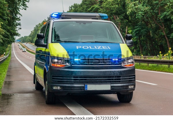 Police car from Germany from\
the state of Brandenburg on the autobahn. Switched on blue light\
and warning lights on the vehicle. Two-lane carriageway in wet\
weather