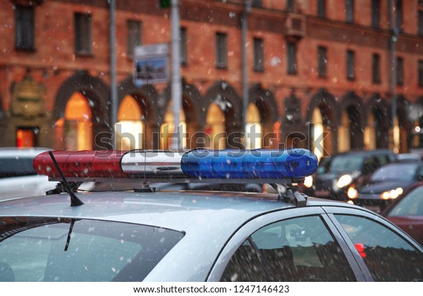Police car on duty during snow storm in snowy\
city. Patrol car, blue and red light siren. Police patrol the\
streets. Engaged in the prevention of violations. Engaged in the\
prevention of\
violations.