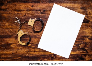 Police Handcuffs And Blank Paper On Investigator Detective's Work Desk, Concept Of Law And Crime.