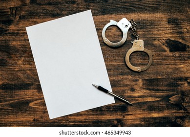 Police Handcuffs And Blank Paper On Investigator Detective's Work Desk, Concept Of Law And Crime.