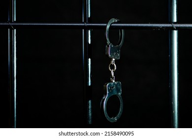 Las esposas de la policía están pegadas a las barras de la celda para los prisioneros con un fondo oscuro, enfoque selectivo.