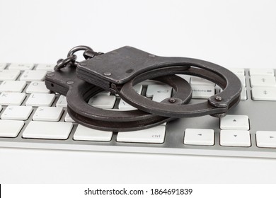 Police Handcuffs Lie On A Computer Keyboard. May Serve As A Symbol Of The Fight Against Cybercrime