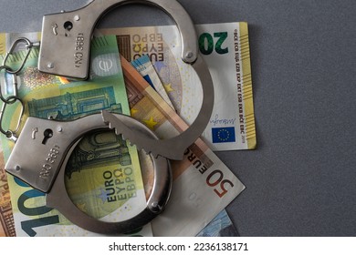 Police handcuffs lies on a set of green monetary denominations of 100 euros. A lot of money forms an infinite heap - Shutterstock ID 2236138171