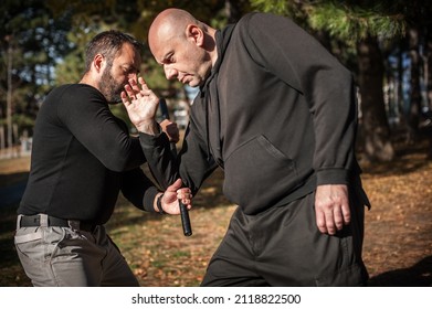 Police instructor demonstrates fighting, apprehension and arrest techniques using a police baton, outdoor in public park. Rubber baton, truncheon or nightstick