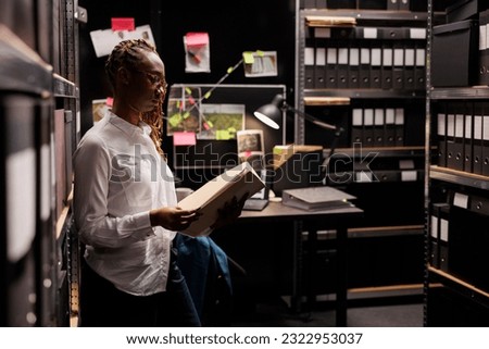 Police investigator reading crime case near files storage at night time. African american woman lawyer searching information in archive shelf and analyzing forensic expertise report