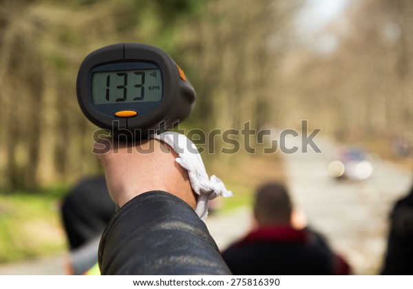 A police man hand\
pointing radar gun at speeding car.Concept:\
Crime,Speeding,traffic,surveillance
