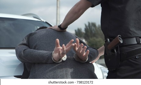 Police officer arresting criminal, putting him on car trunk and reading rights for him.