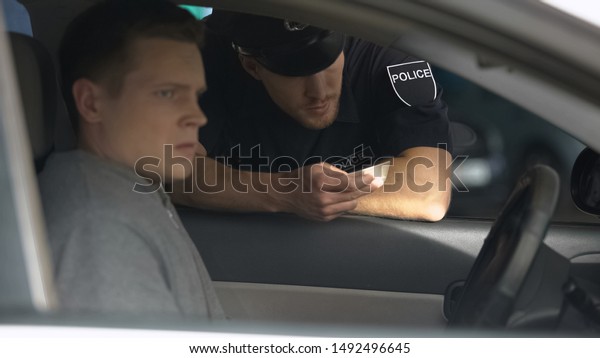 Police officer checking documents of nervous man in\
car, traffic control,\
rules