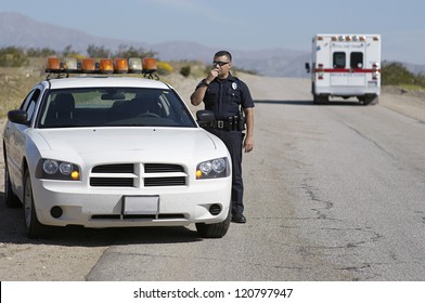 Police Officer Communicating On Radio Standing By Car