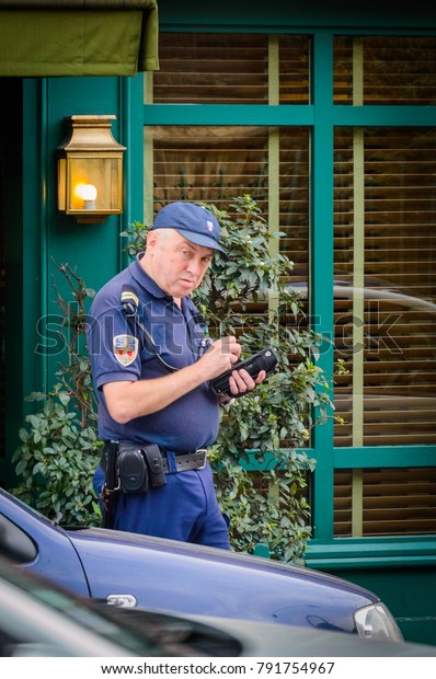 Police officer giving a ticket\
fine for parking violation. The policeman checks the parking time\
of the car in paid street parking. Paris, France, October 04,\
2014