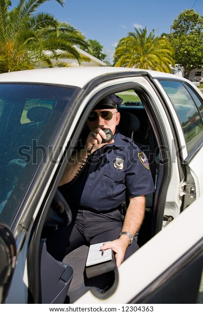 Police officer in his car calling in a license\
number on his radio.
