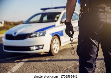 Police Officer Holding Handcuffs, Police Car In Background.