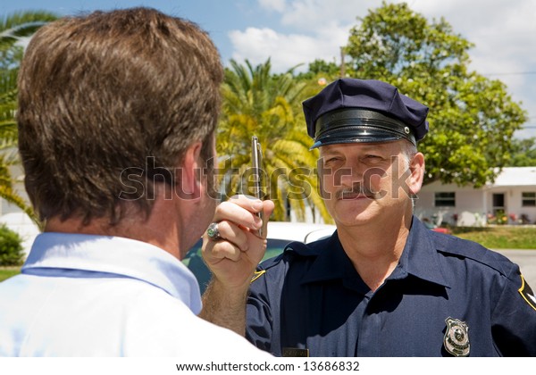 Police officer holding a pen and doing a field\
sobriety test on a\
motorist.
