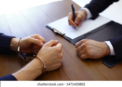 Police Officer Interrogating Criminal In Handcuffs At Desk Indoors